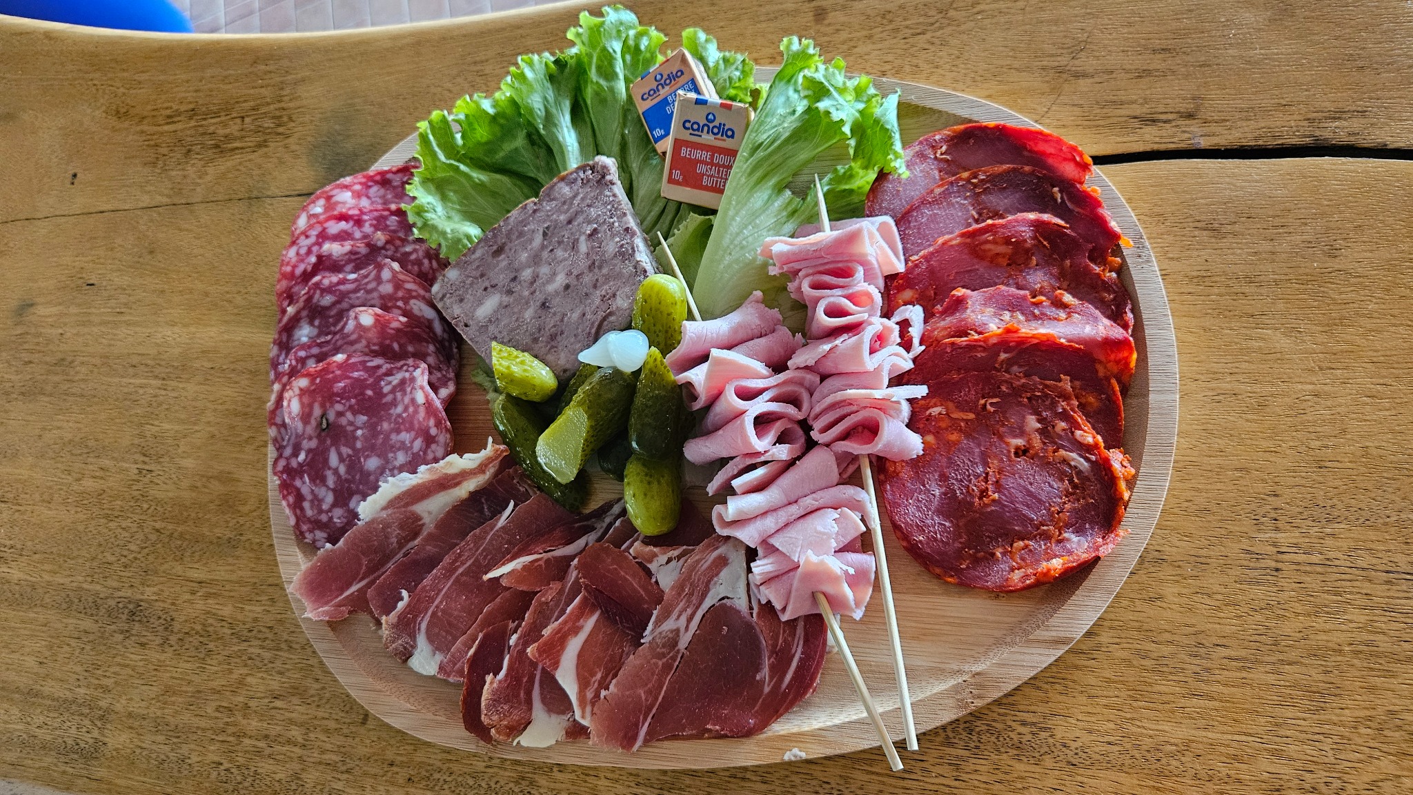 Planche de charcuteries, cornichons et salade servie sur une table en bois