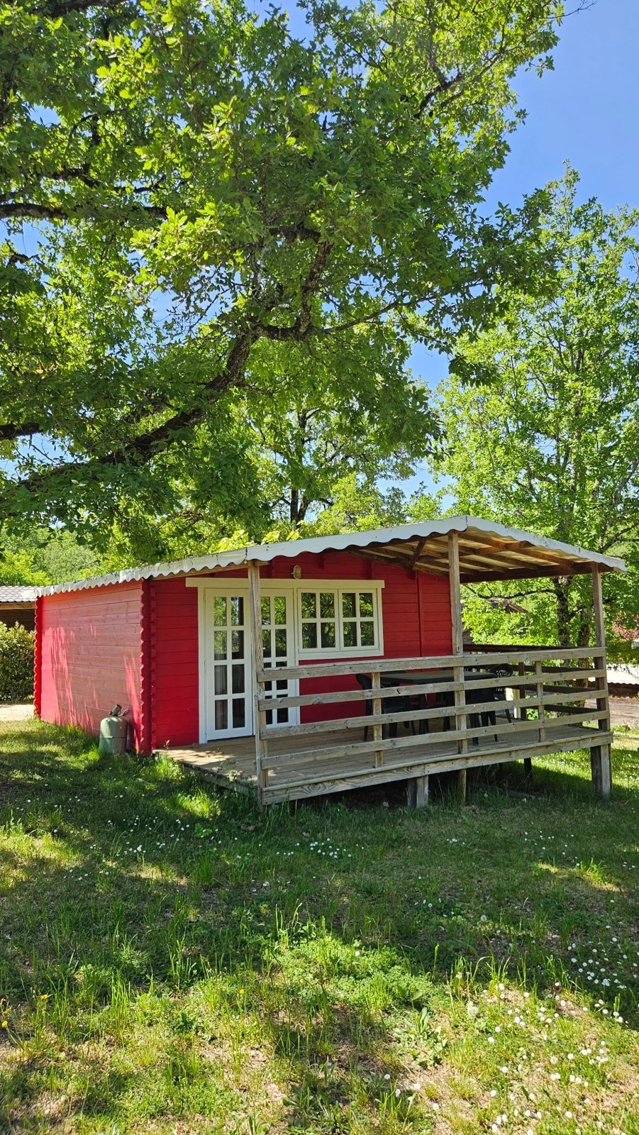Chalet rouge du Camping Ohana, sa terrasse et les arbres tout autour