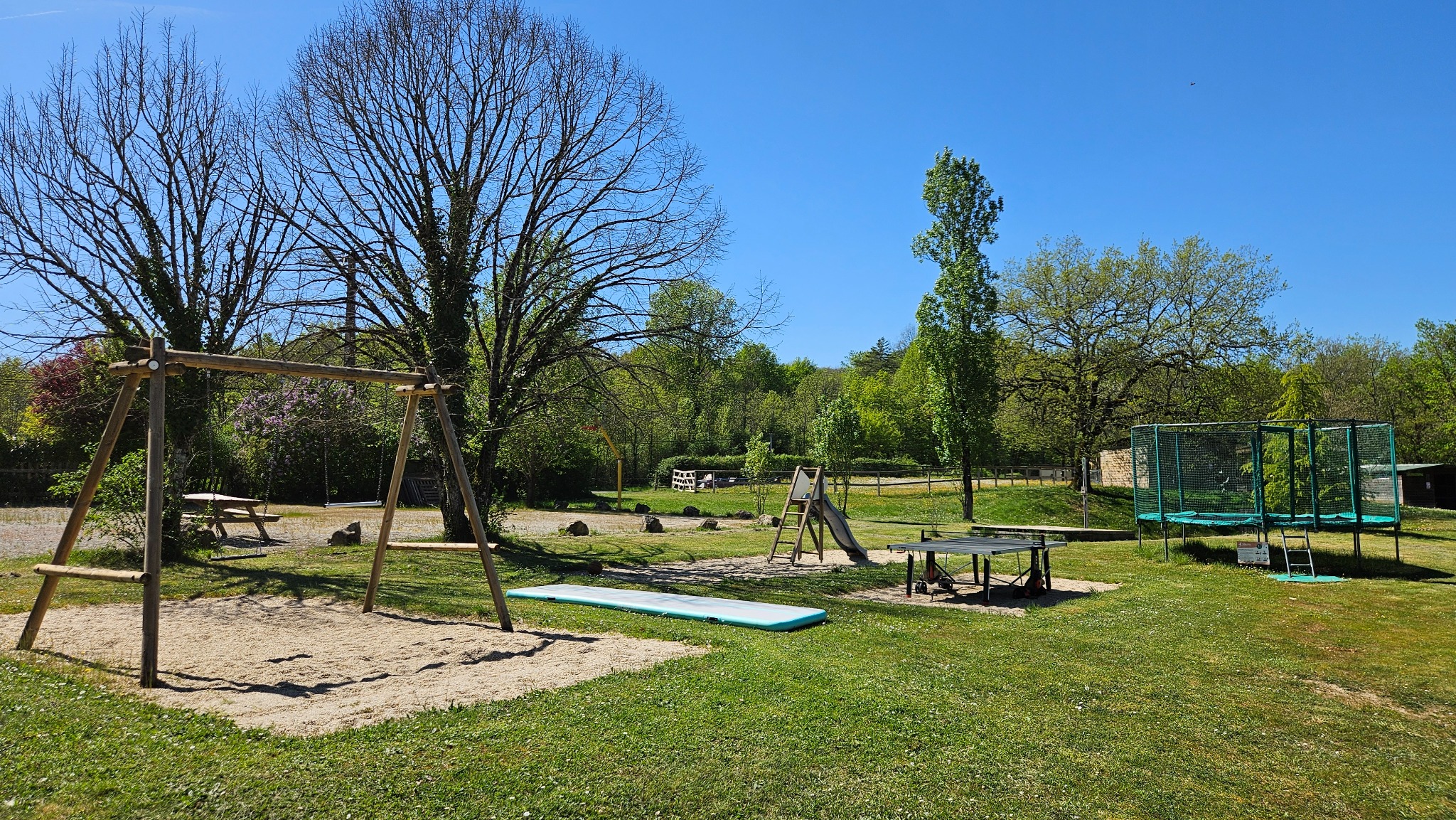 Vue du parc de jeux du Camping Ohana avec balançoires, toboggan, table de ping-pong et trampoline