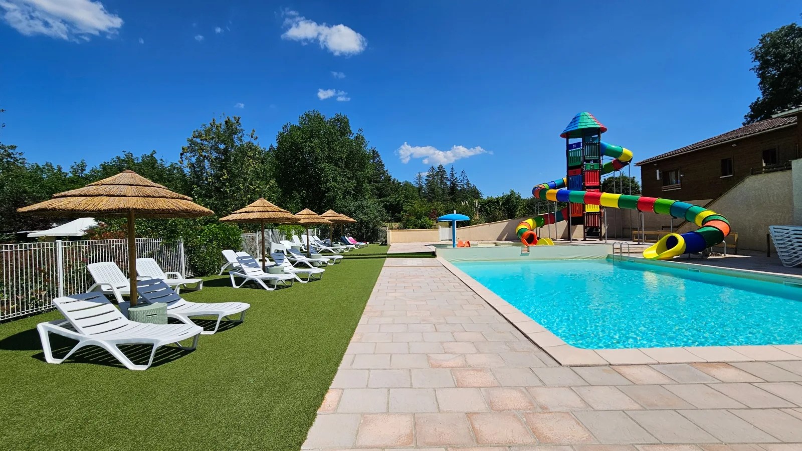 La piscine du Camping Ohana, les transats et les toboggans colorés dans un cadre boisé