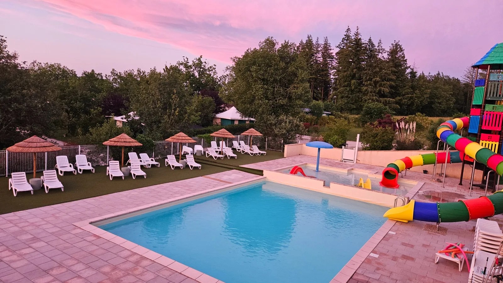 La piscine et les toboggans du Camping Ohana sous un ciel rose en soirée