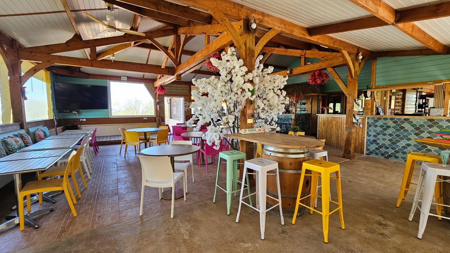 Salle lumineuse du Camping Ohana avec tables, banquettes et décor floral